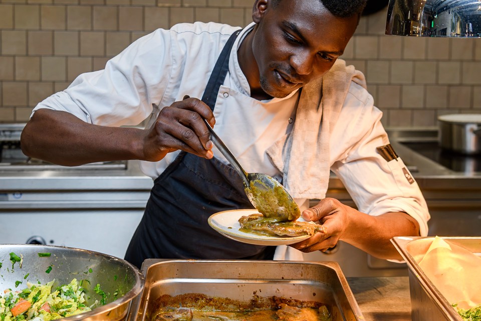 A chef carefully spoons food onto a plate in the kitchen at A Beautiful Mess.