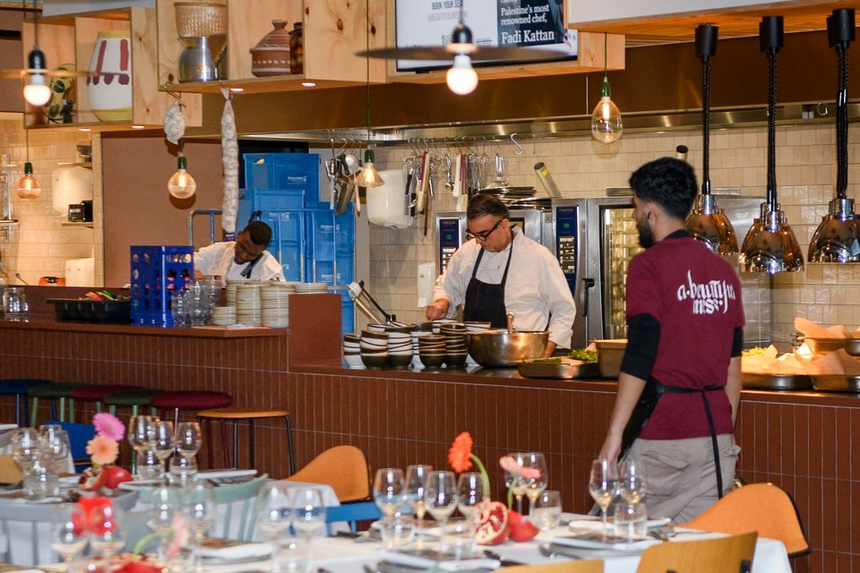 Cooks and a member of the service team at the open kitchen counter, with set tables in the foreground.