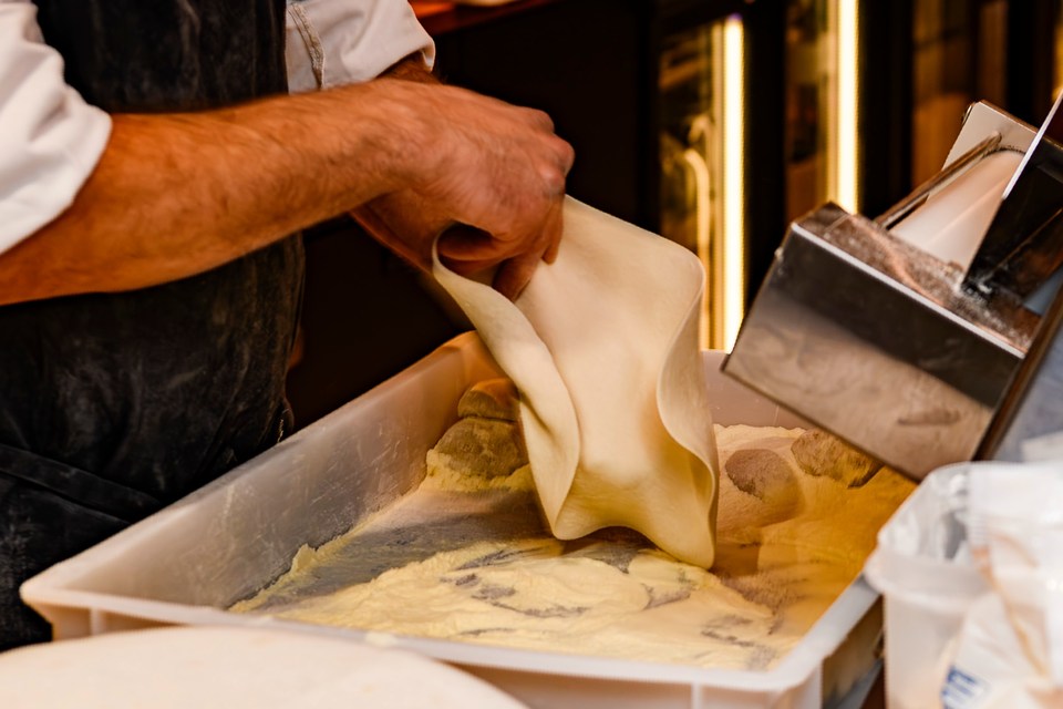 Flour-dusted hands stretch dough beside a work surface.