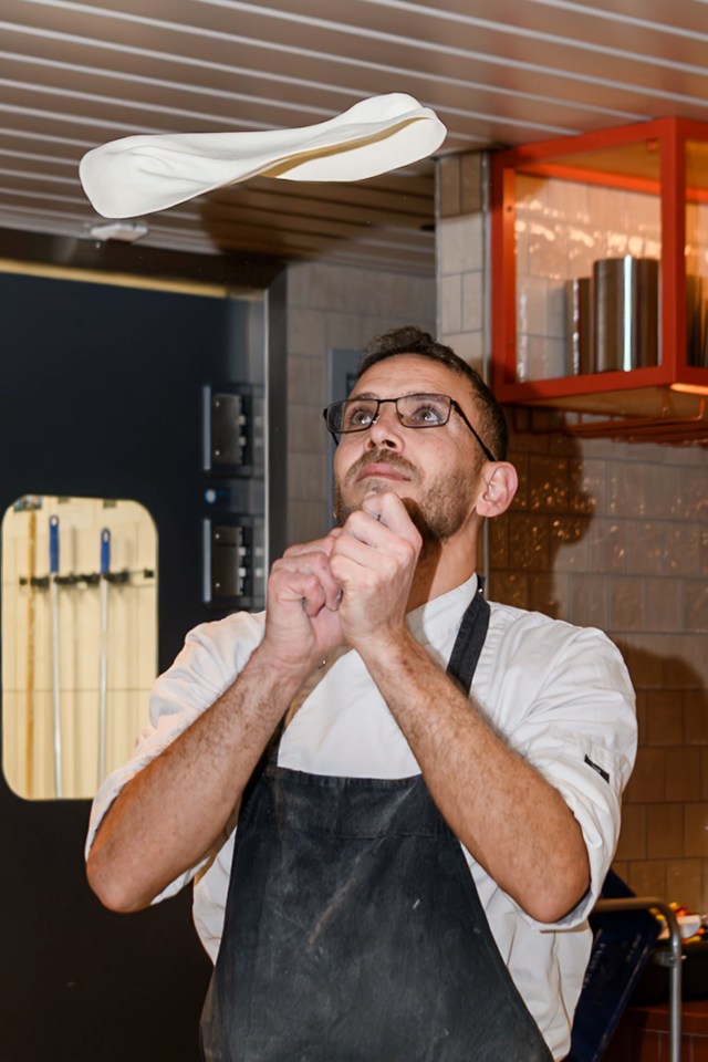 A cook looks up at a round of dough tossed above his hands.