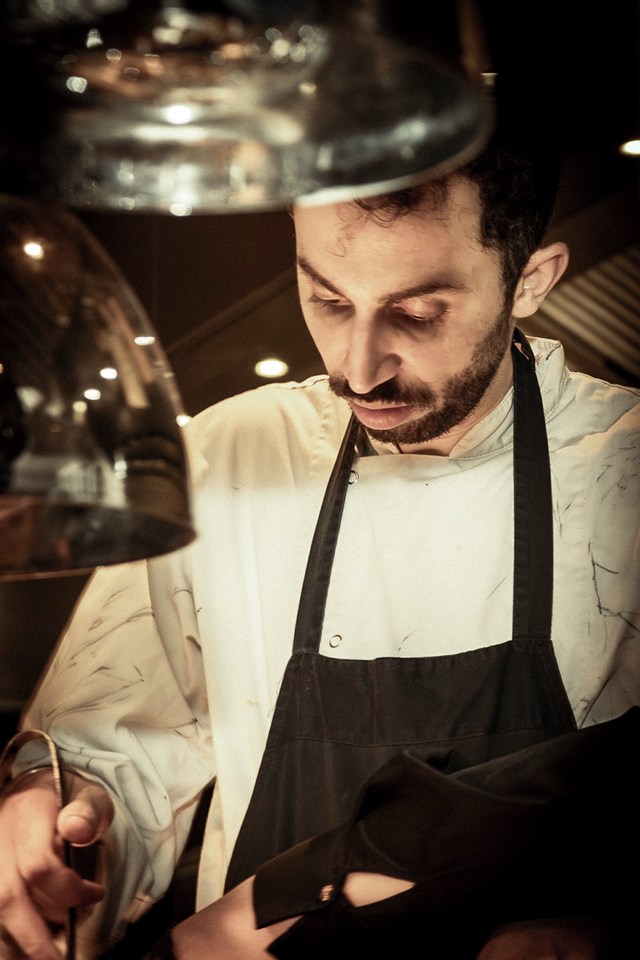 A cook concentrates on his work beneath the reflective kitchen lamps.