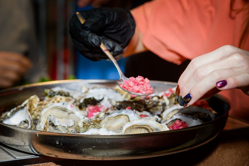 Hands add a bright pink garnish to oysters on a serving tray.