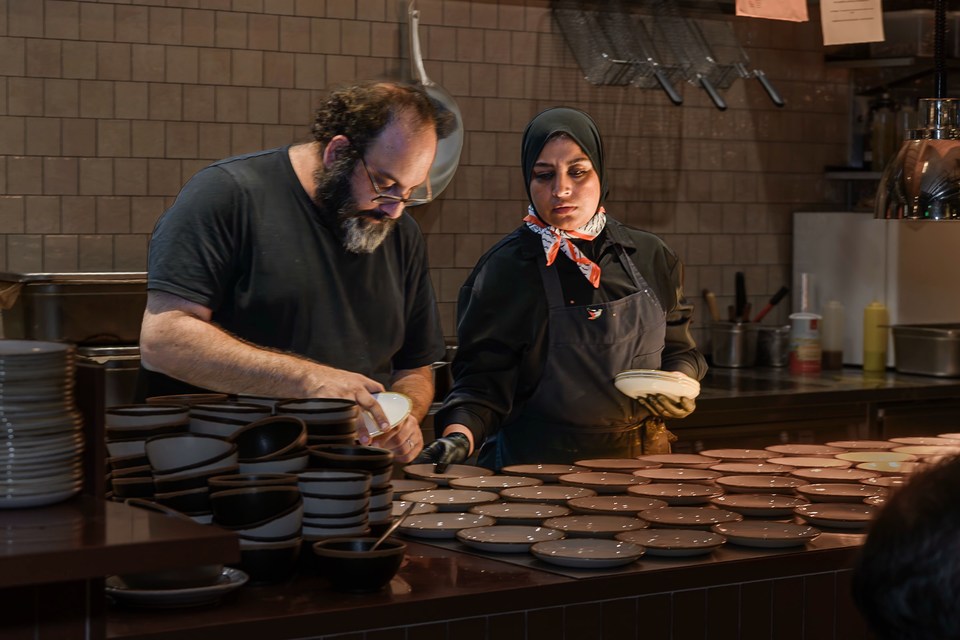 Two cooks work together across rows of plates and bowls.
