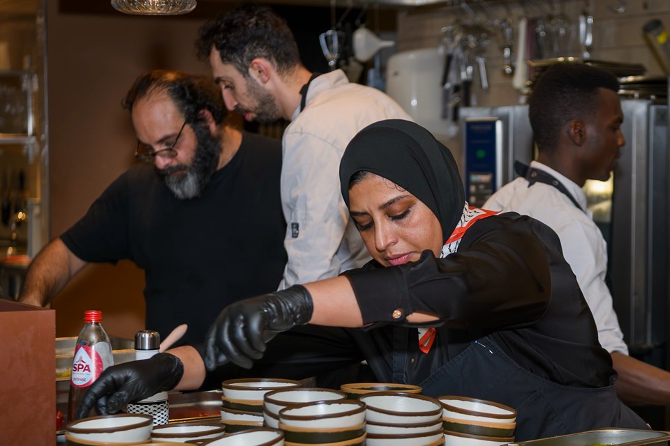 A cook reaches across rows of bowls while colleagues work behind her.