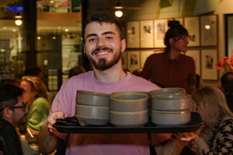 A smiling member of the service team holds a tray of bowls.