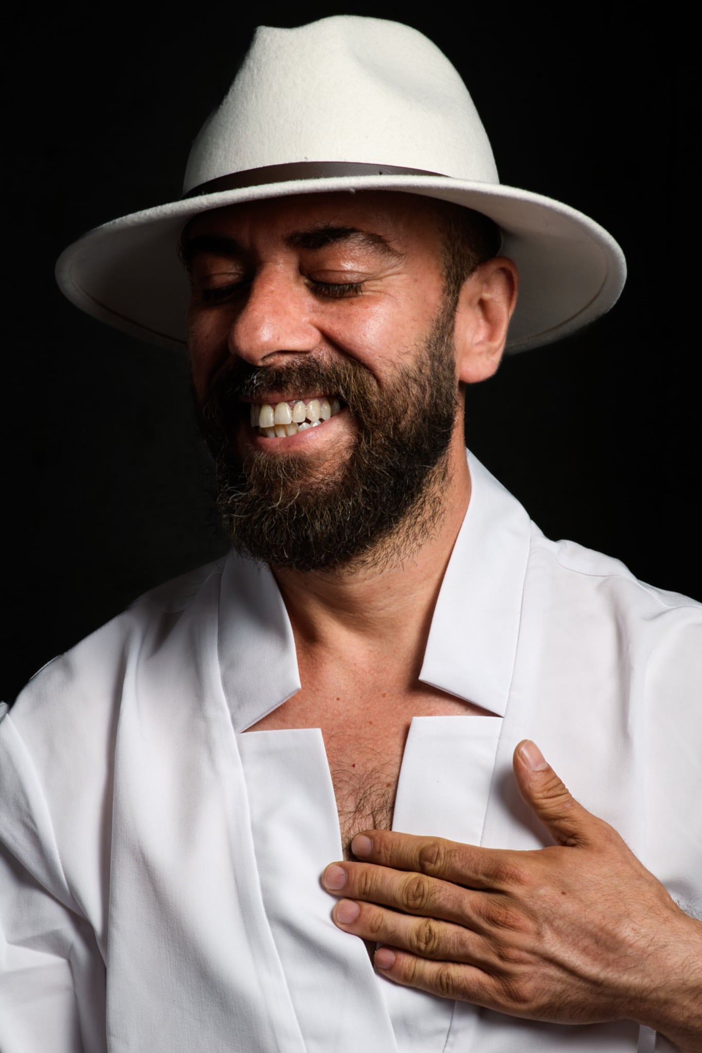 A smiling bearded man in a white hat and open white shirt