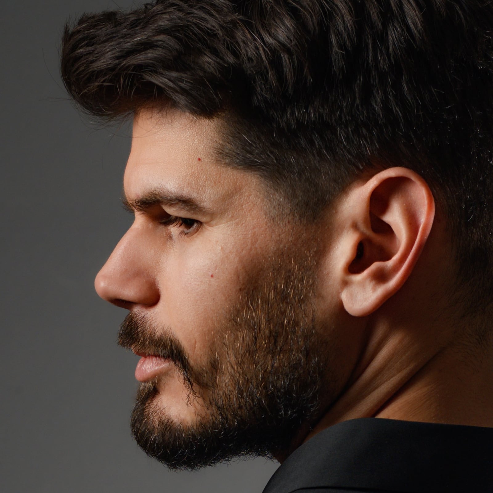 Colour profile portrait of a dark-haired man facing left against a grey background