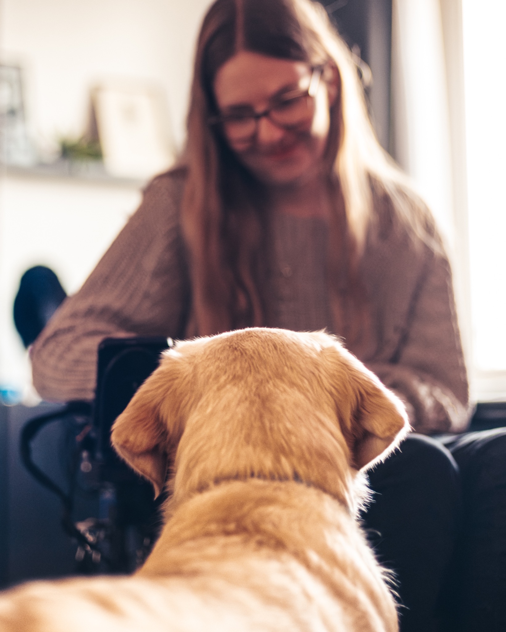 Een assistentiehond kijkt naar een lachende vrouw in haar huis