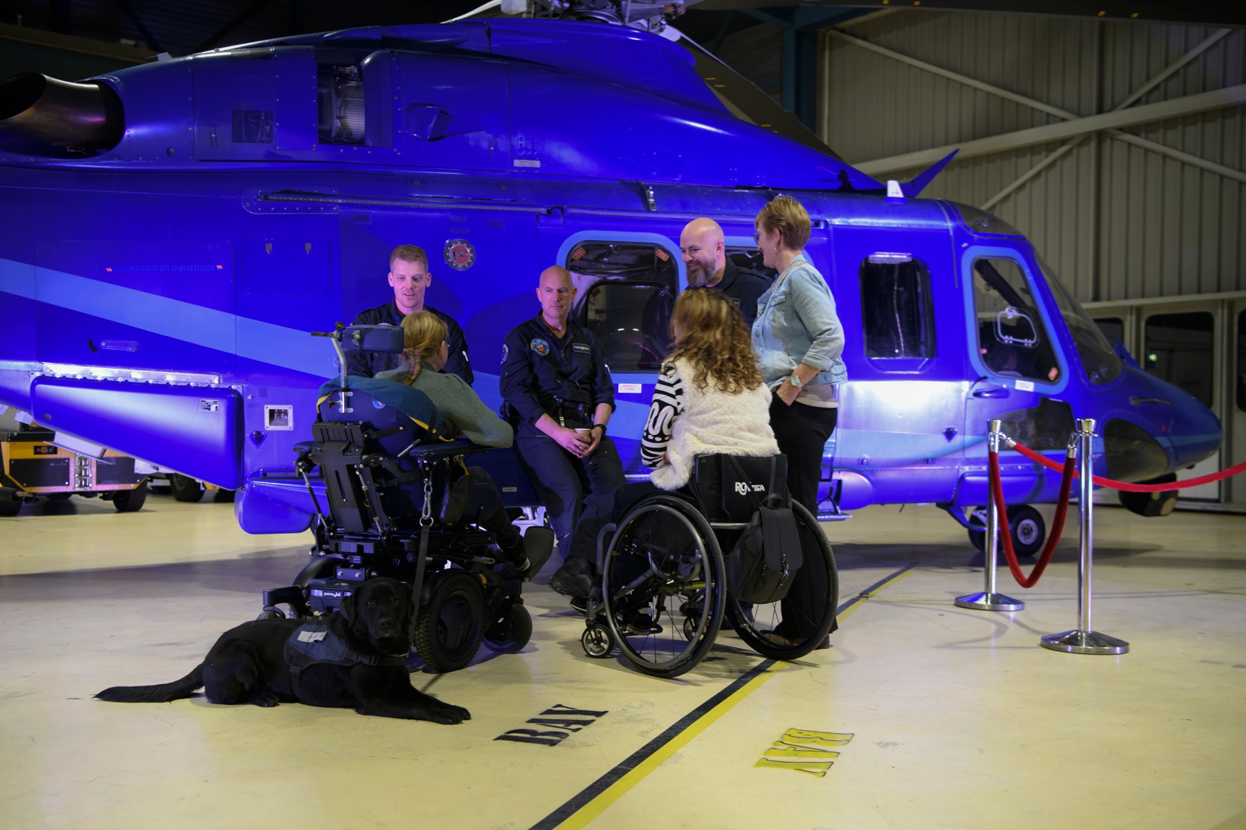 People, wheelchairs and a dog gathered in front of a helicopter.