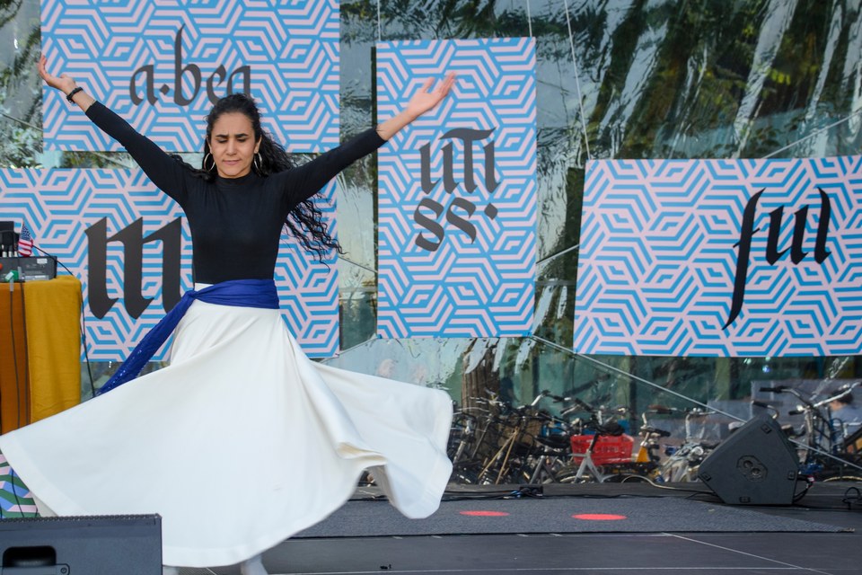 A dancer extends her arms as her white skirt moves across the stage.