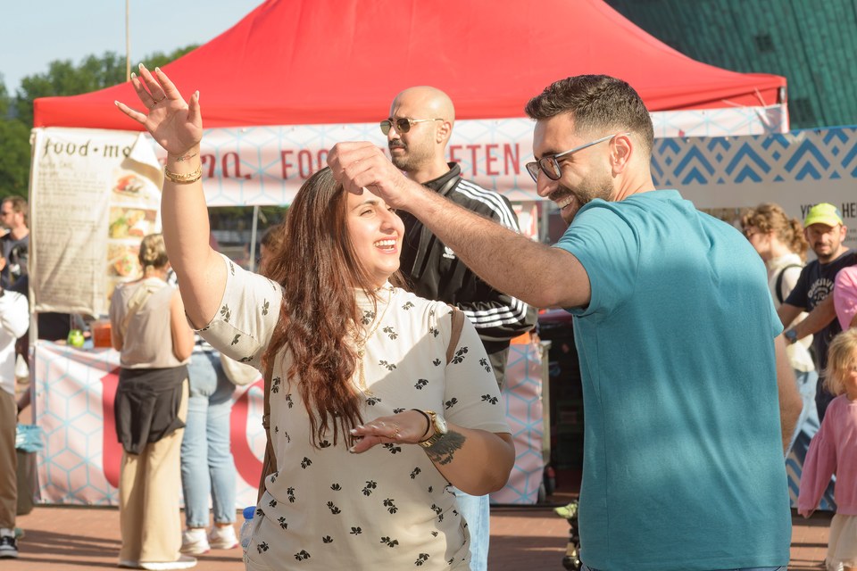 People dance together in the sunshine beside the food stalls.