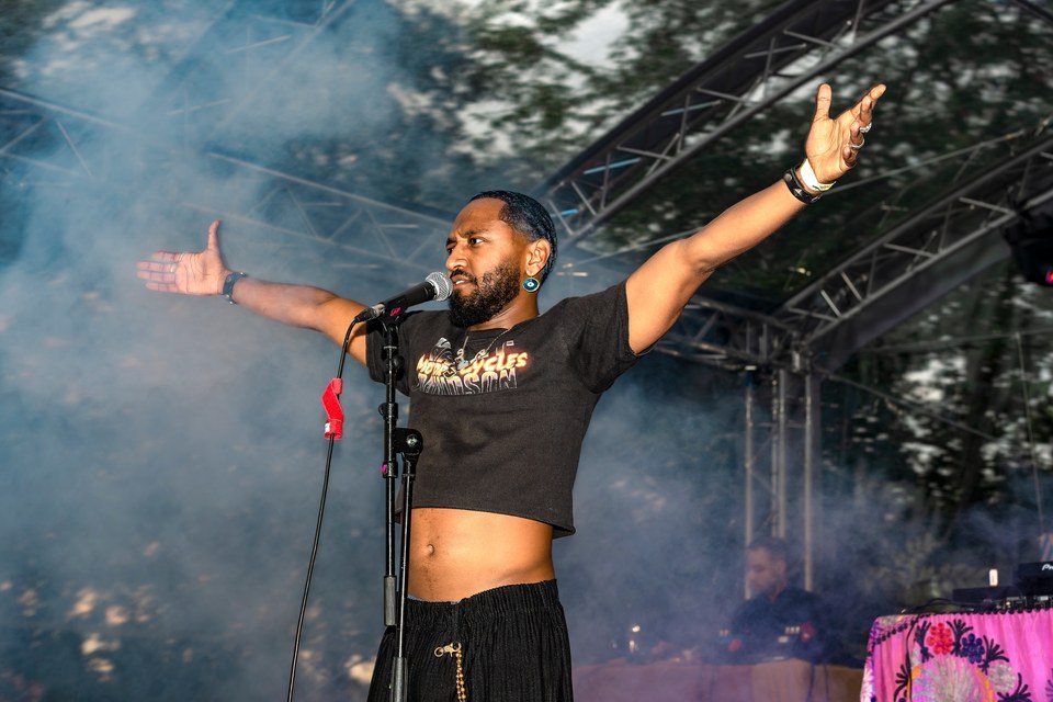 A singer stretches both arms wide amid stage haze.