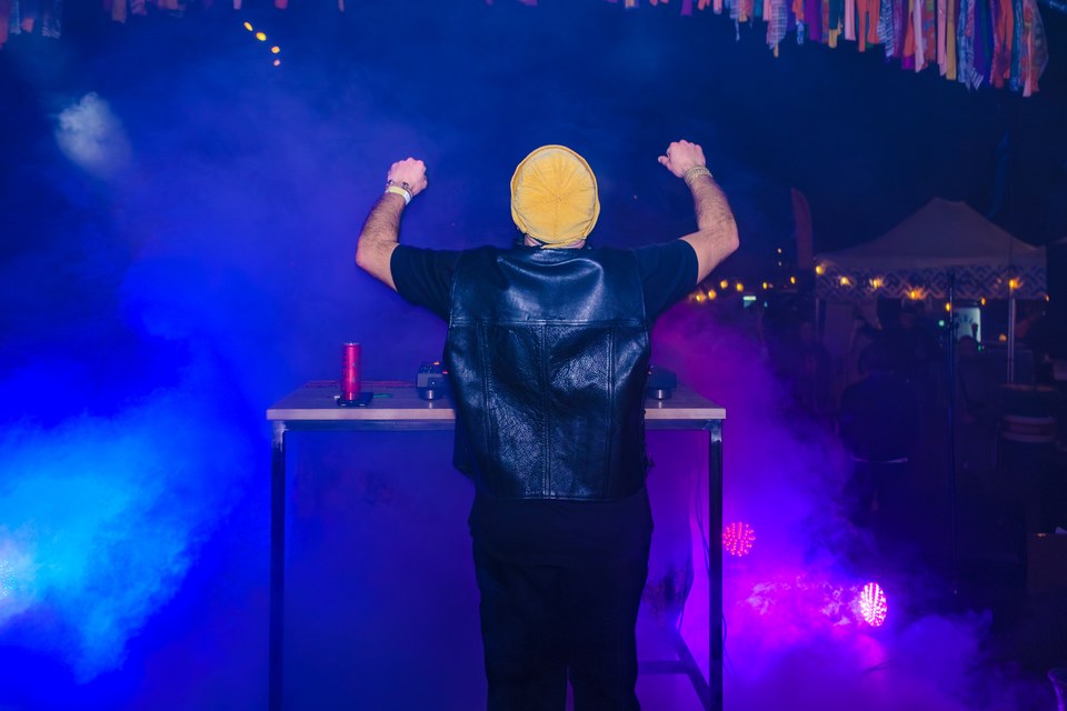 A DJ raises both arms towards the audience through blue stage light.