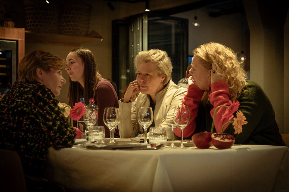 Guests lean into conversation around a warmly lit dining table.