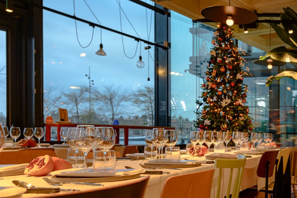 Set tables and a Christmas tree beside the restaurant windows at dusk.
