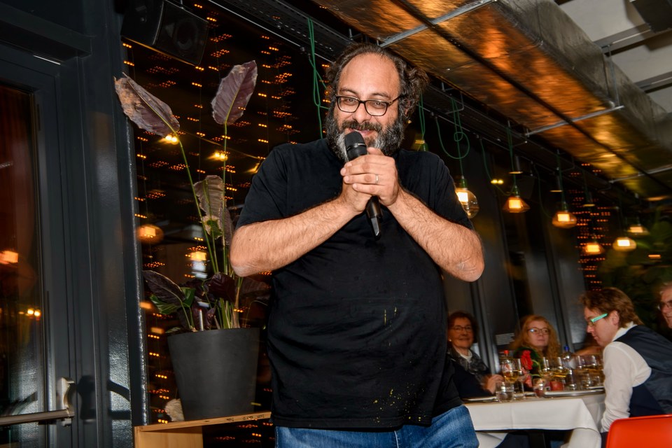 A speaker holds a microphone beside the warmly lit dining room.