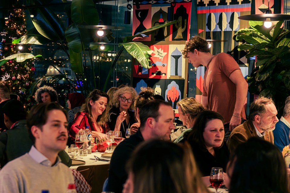 A member of the team leans towards guests beneath colourful artwork and plants.