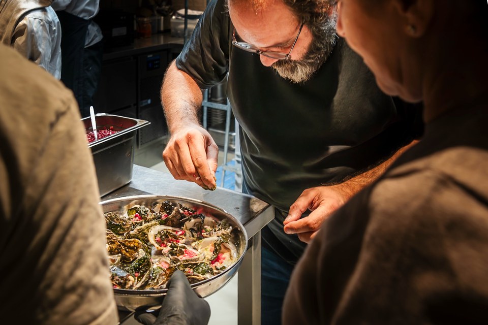 A chef finishes a tray of oysters as people look on.