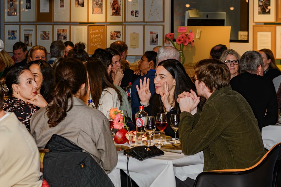 Guests gesture and talk across a crowded dining table.