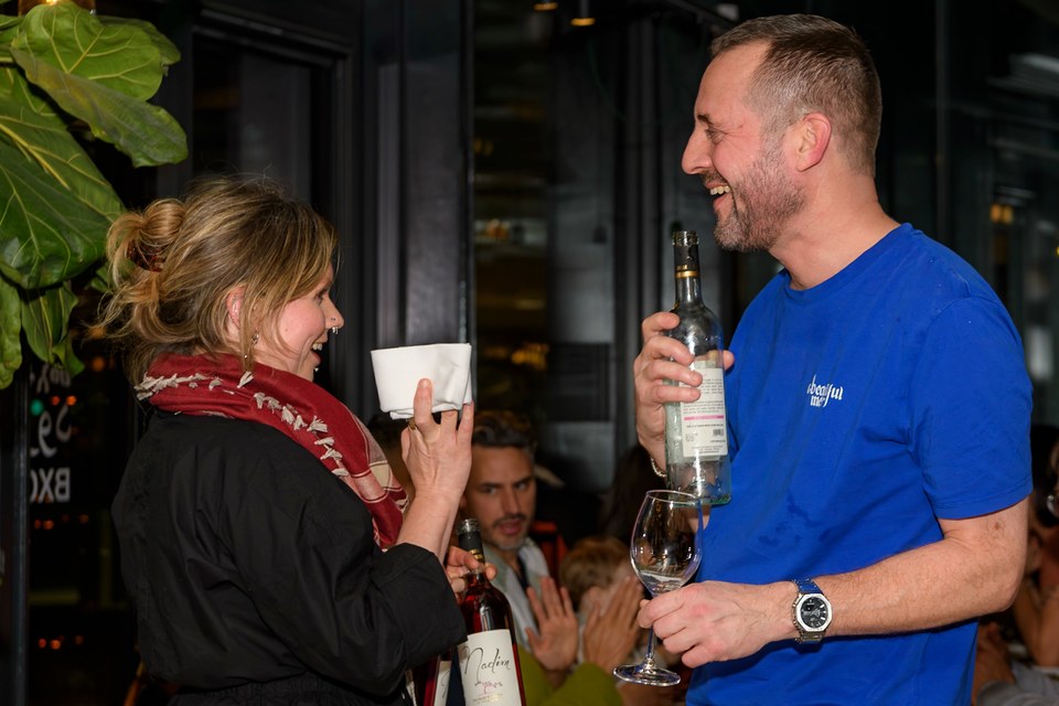 Two people smile together with a cup and a bottle beside the dining room.