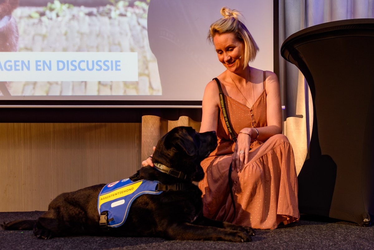 A woman sits beside an assistance dog near the stage.