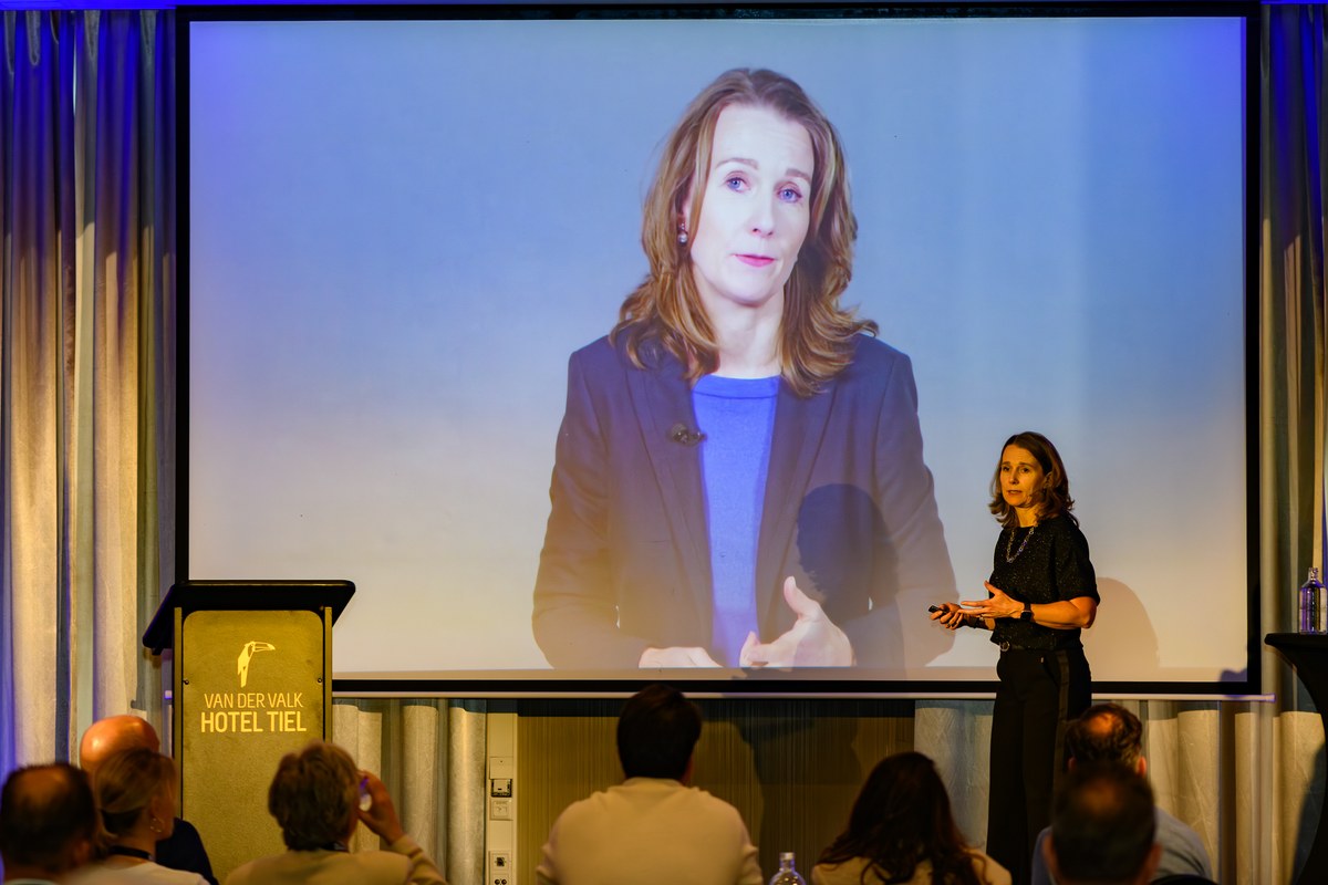A speaker presents beneath a large projected portrait.