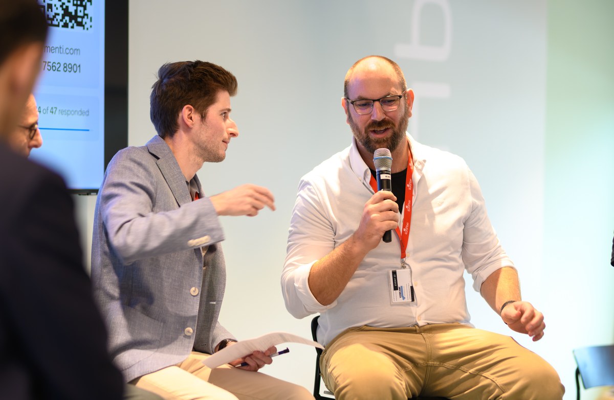 Two seated panellists share an exchange, one holding a microphone.