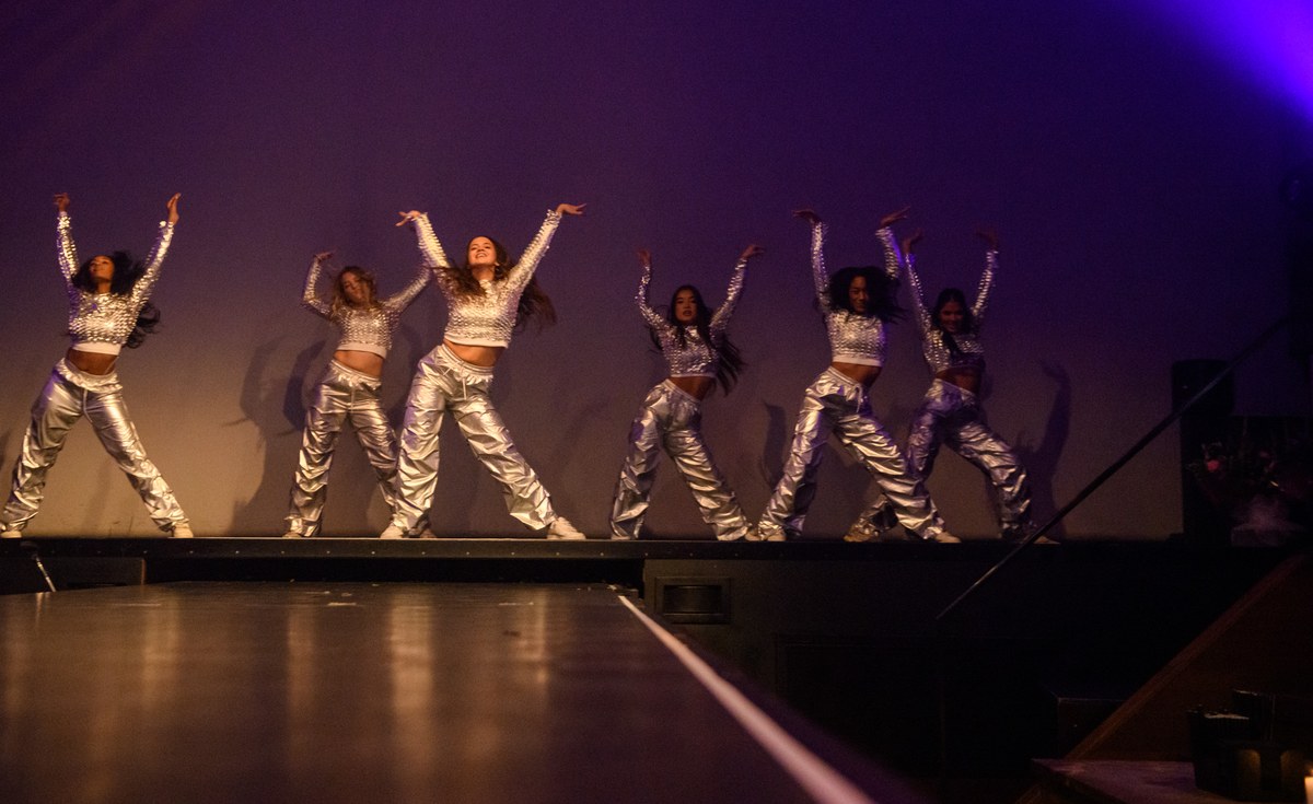 A troupe performs with arms raised on the stage.