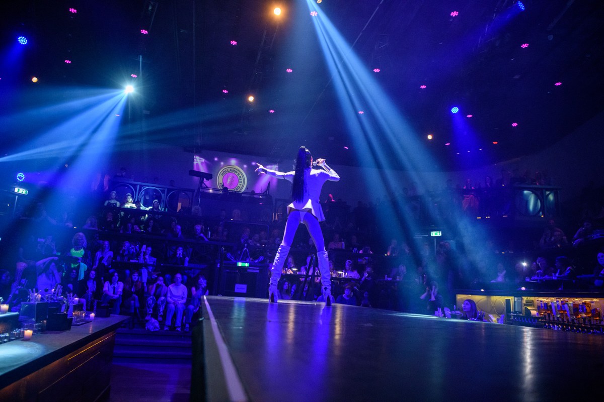 A performer faces the room beneath blue stage lights.