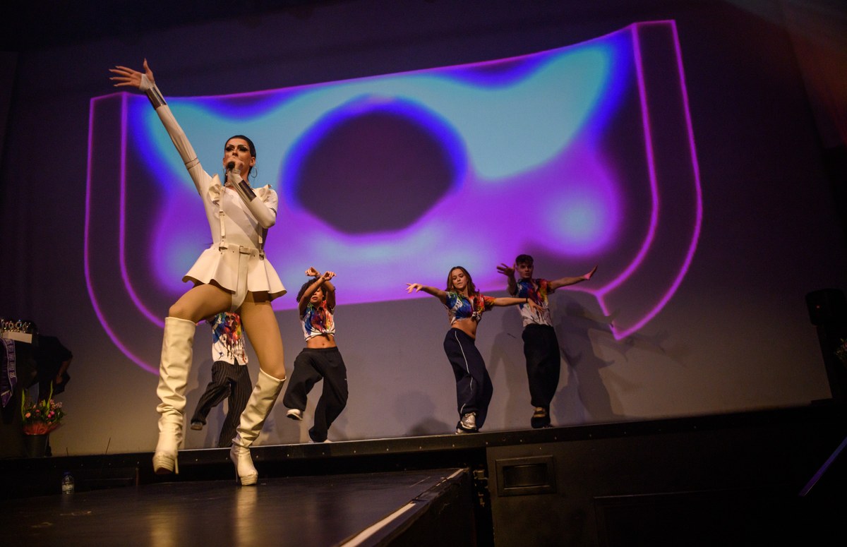 A lead performer raises an arm with dancers behind.
