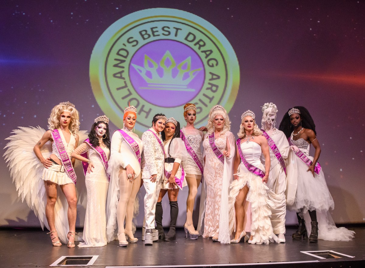 Crowned performers in white and pink pose together beneath the event emblem.