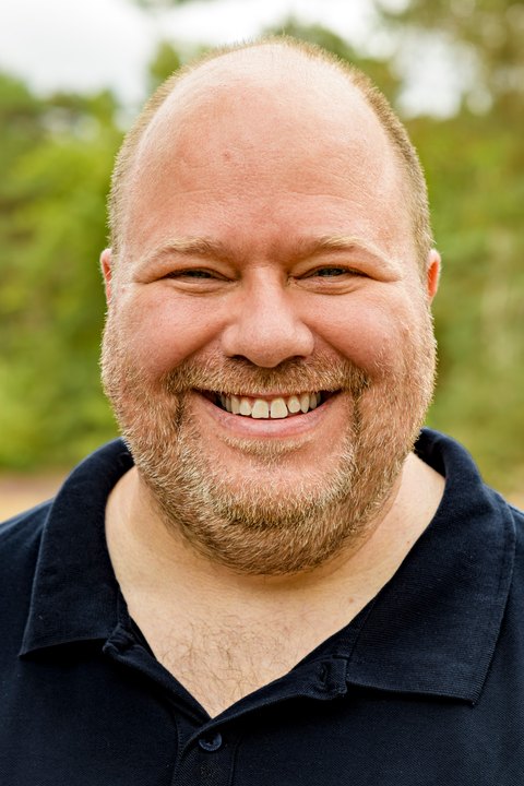 A man smiling broadly towards the camera in a close portrait.