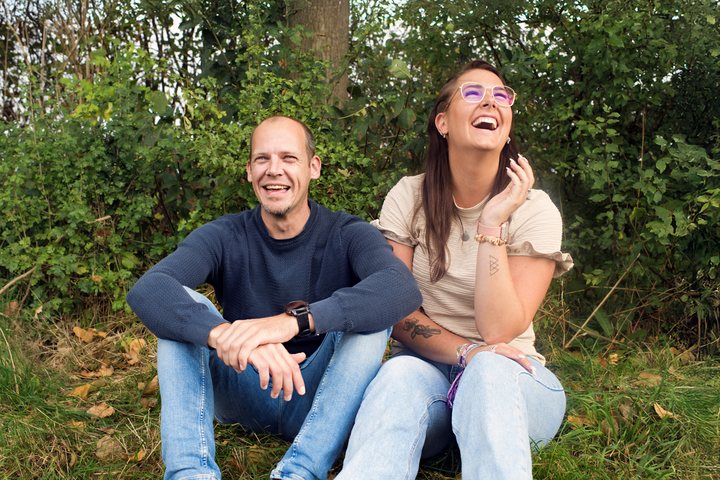 Two people laugh together beneath the trees.