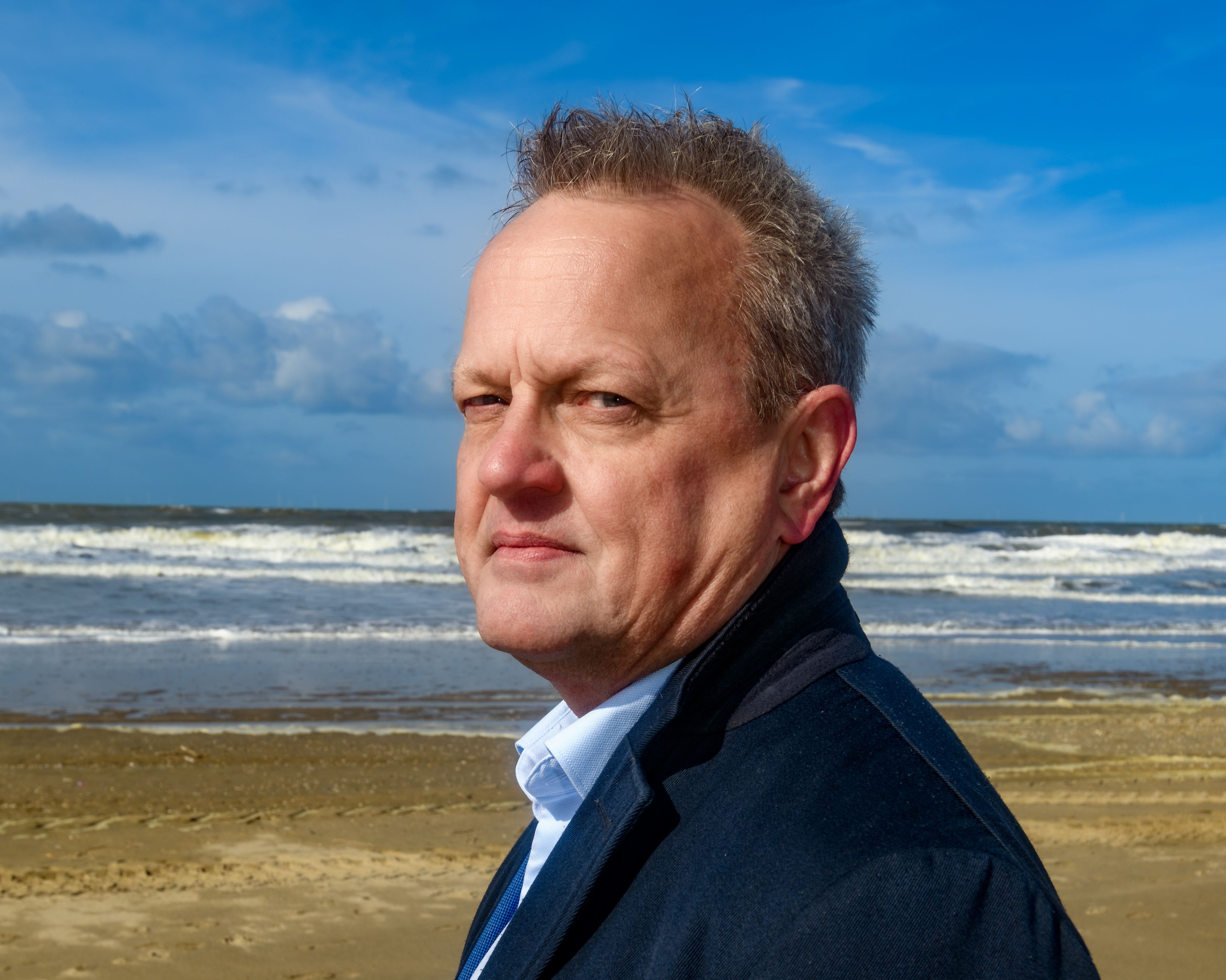 Frank van der Linden op het strand onder een helderblauwe lucht
