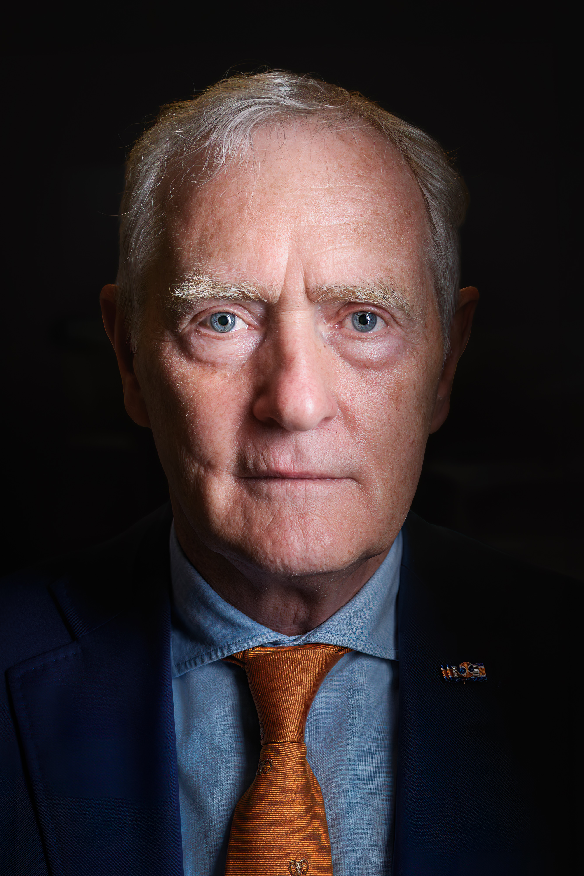 Close-upportret van Peter van Uhm in een blauw pak met oranje stropdas