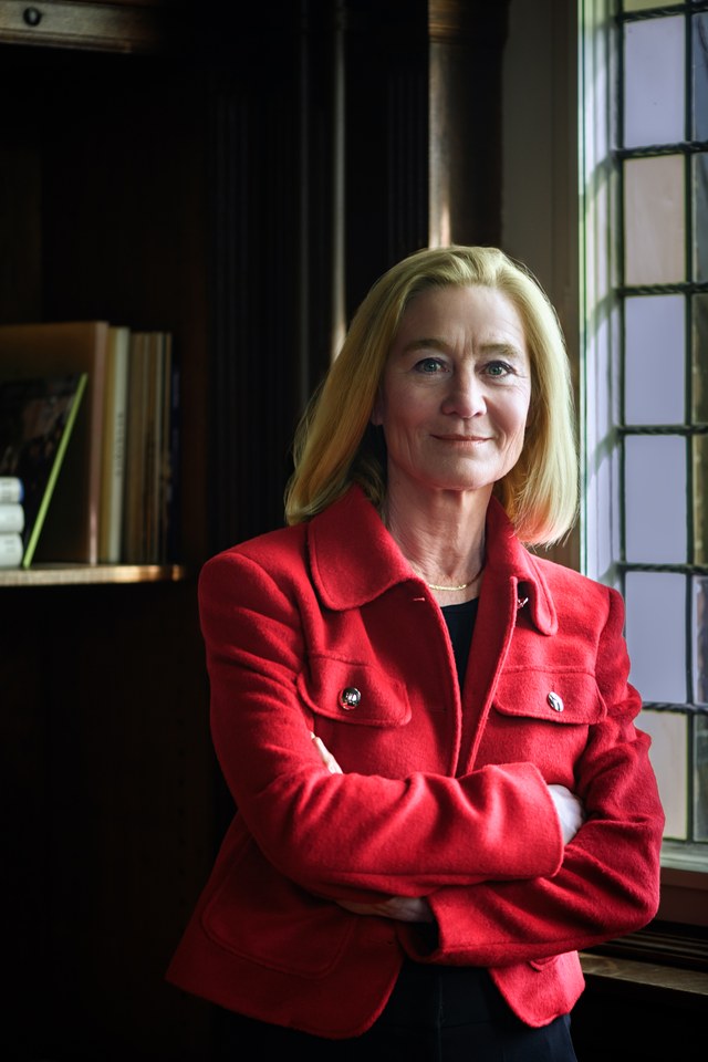 A woman beside a tall window, wearing a red jacket.