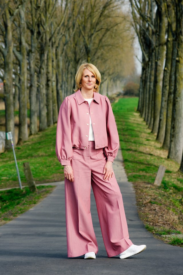 A woman in a pink suit on a tree-lined path.