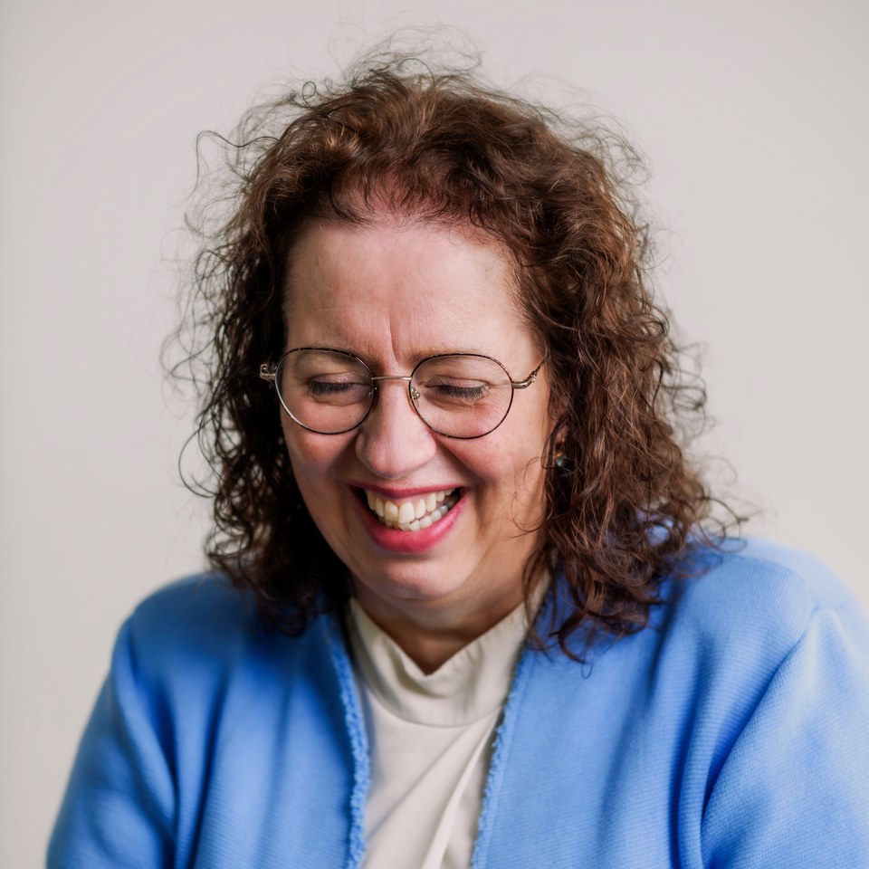A woman in glasses and a blue jacket, laughing naturally.