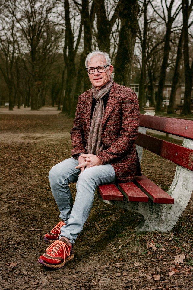 A man in a red textured jacket seated on a red bench in woodland.