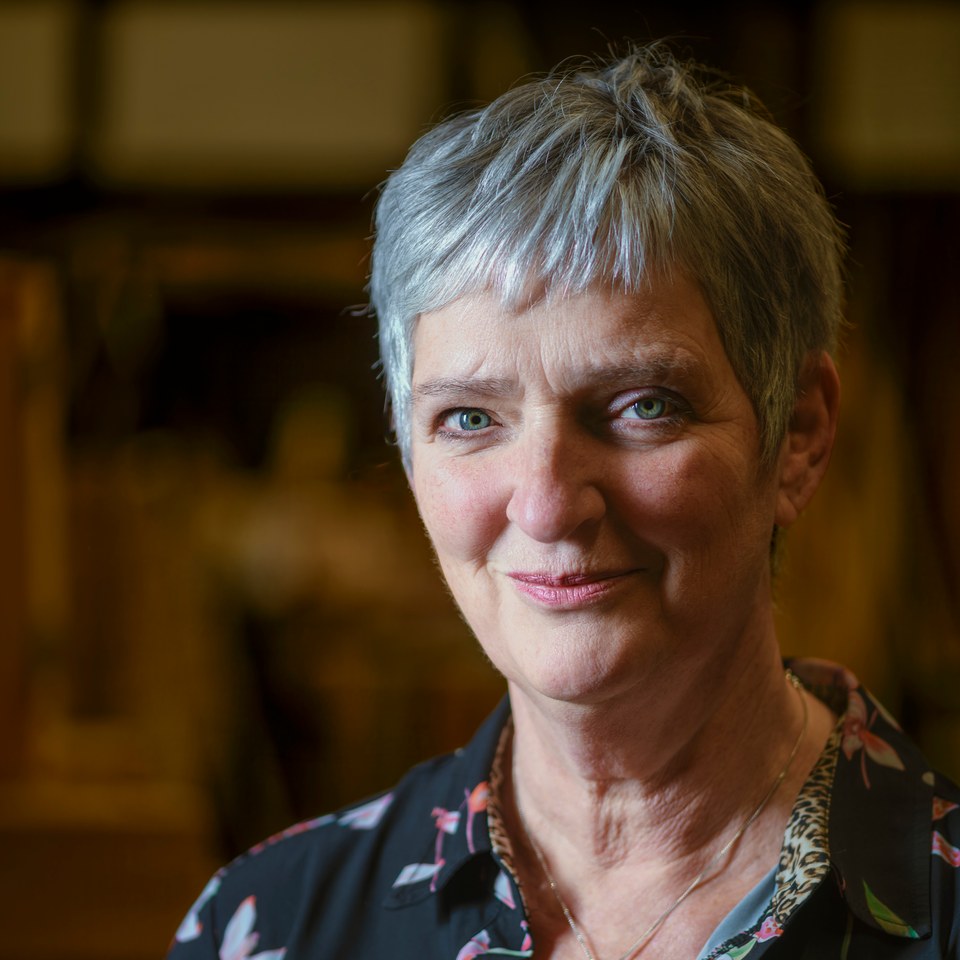 Close portrait of a woman with short grey hair and a subtle smile against a softly blurred workshop.