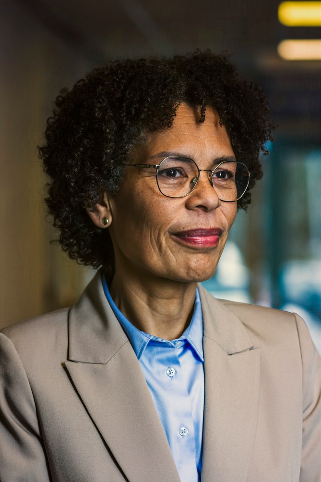 A woman in glasses and a taupe jacket, photographed in three-quarter view.