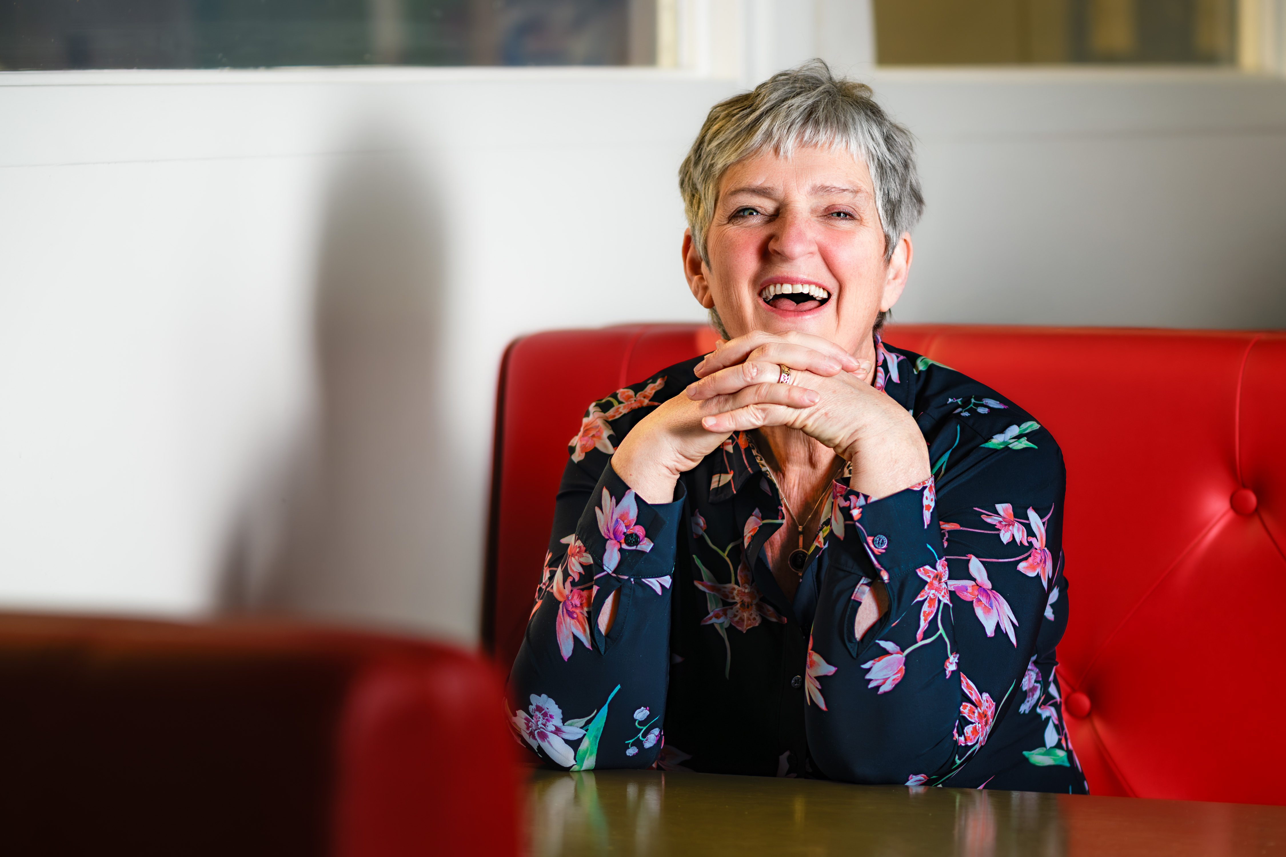 A woman laughing at a table in a red upholstered seat.