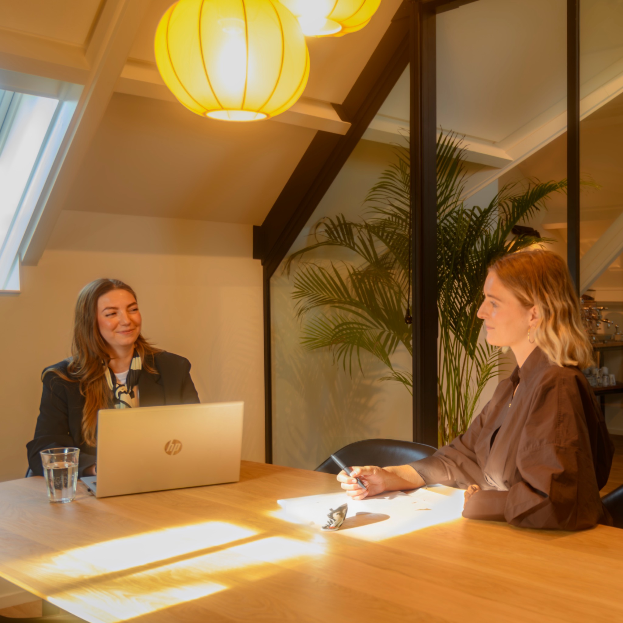 Twee collega’s in gesprek aan een zonovergoten vergadertafel