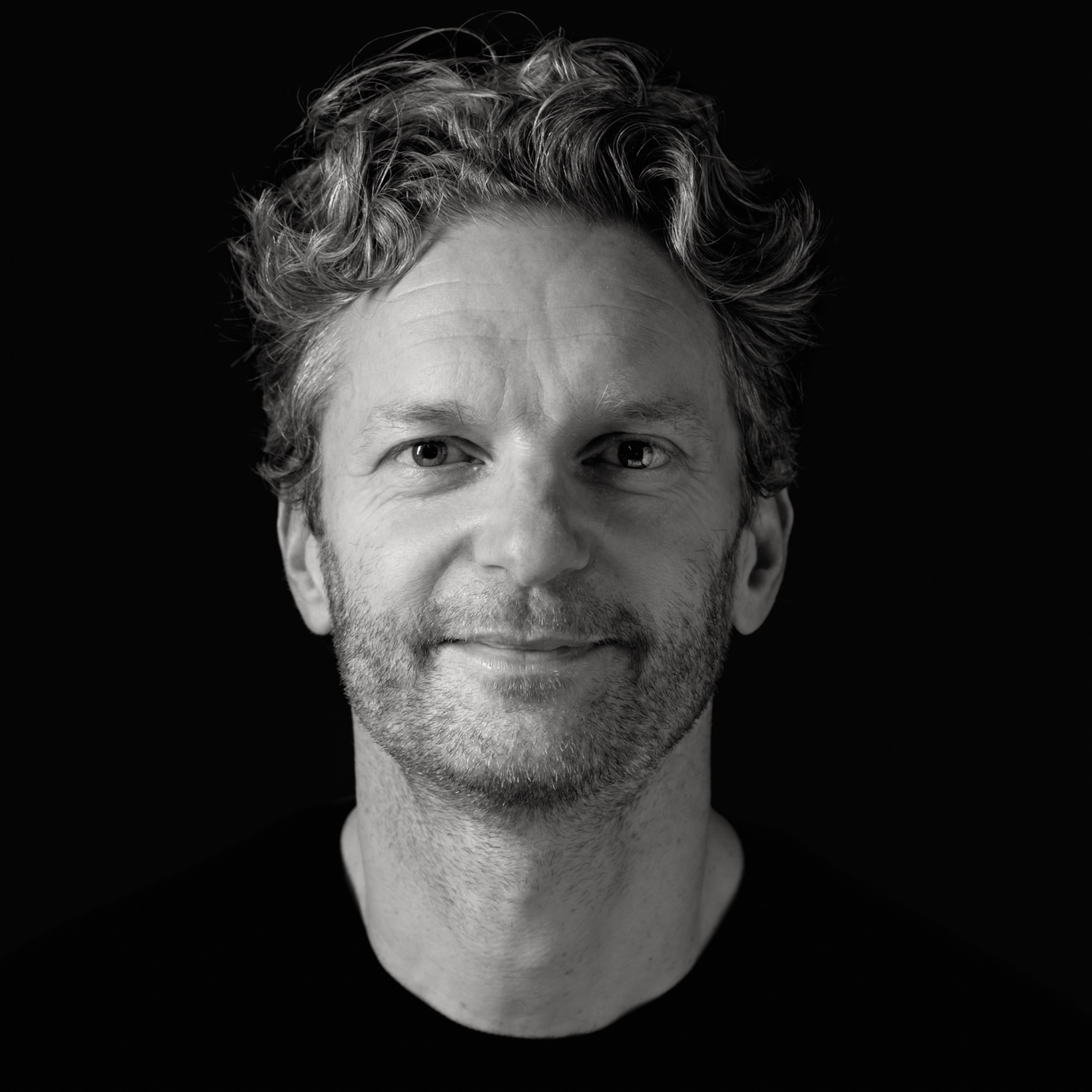 Zwart-wit headshot van een man met licht krullend haar