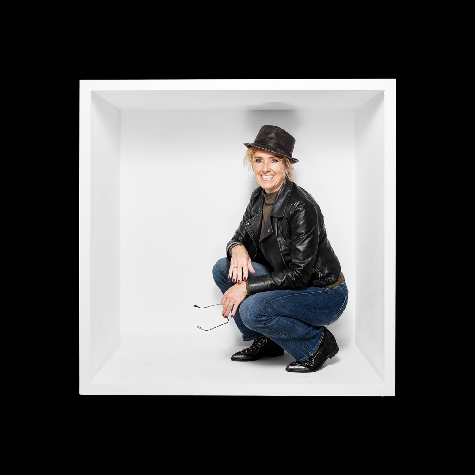 Woman in a dark jacket and hat crouching inside a white box