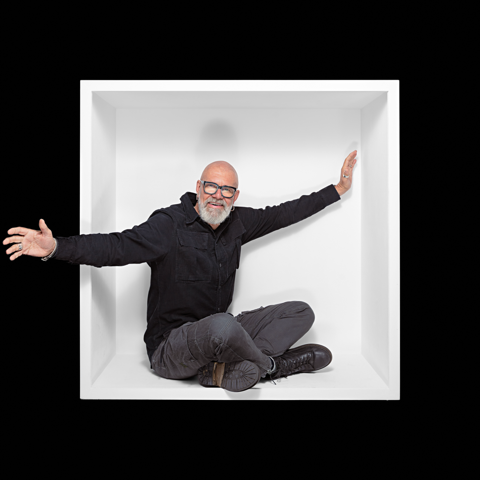 Seated man opening his arms beyond the edges of a white box