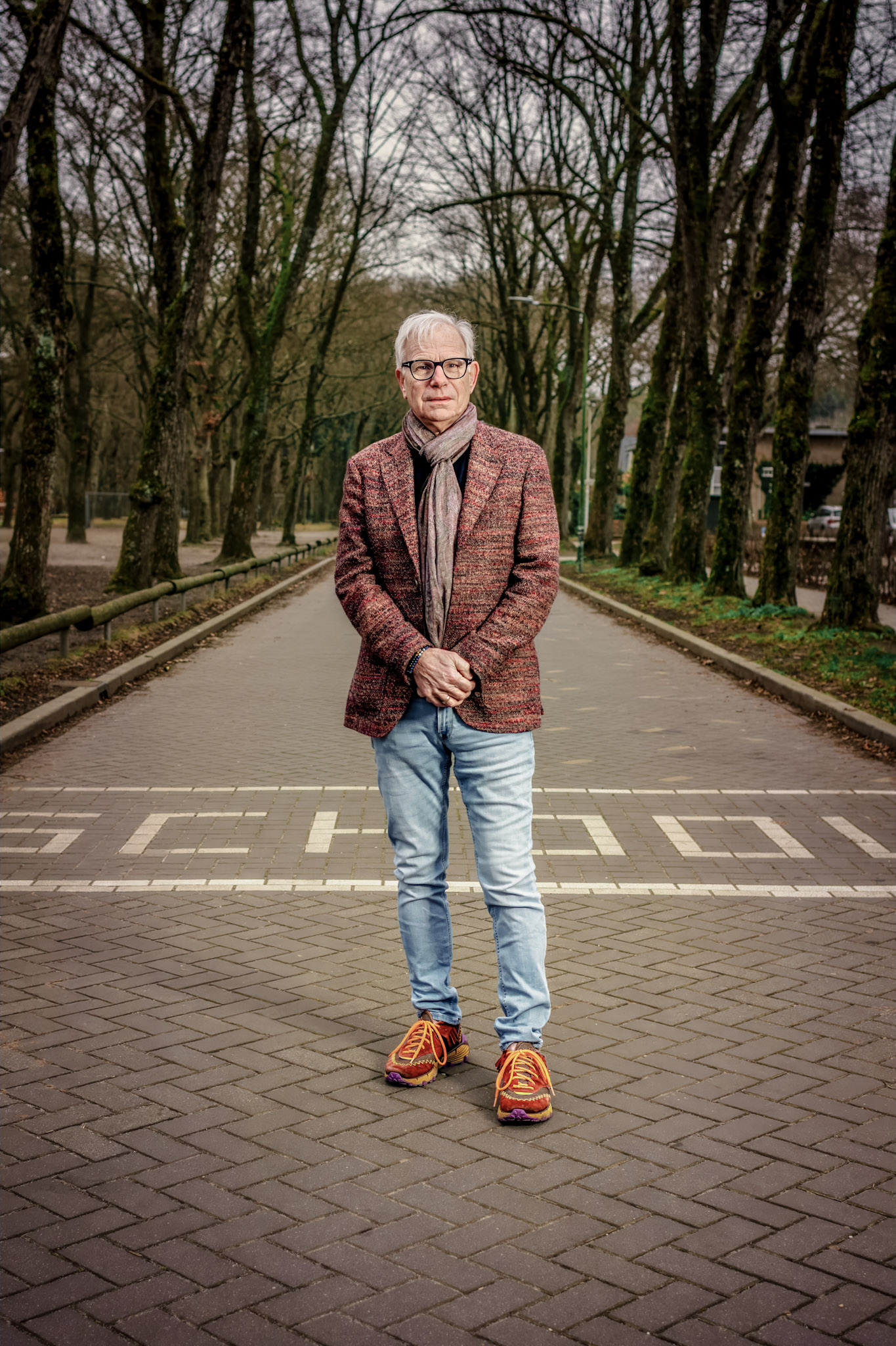 Full-length portrait in a patterned jacket and colourful shoes on a tree-lined path