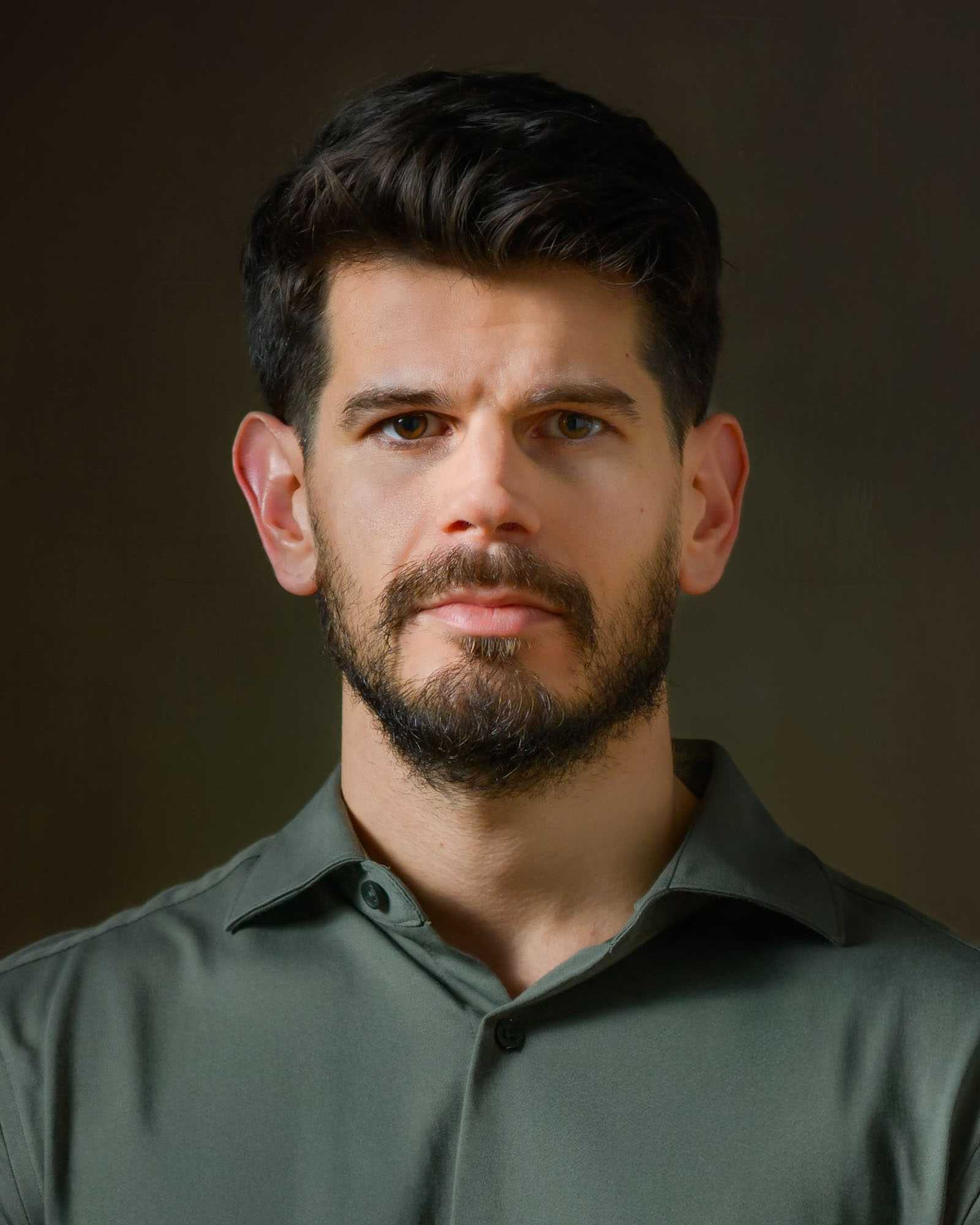 Studio headshot of a dark-haired man in a green shirt