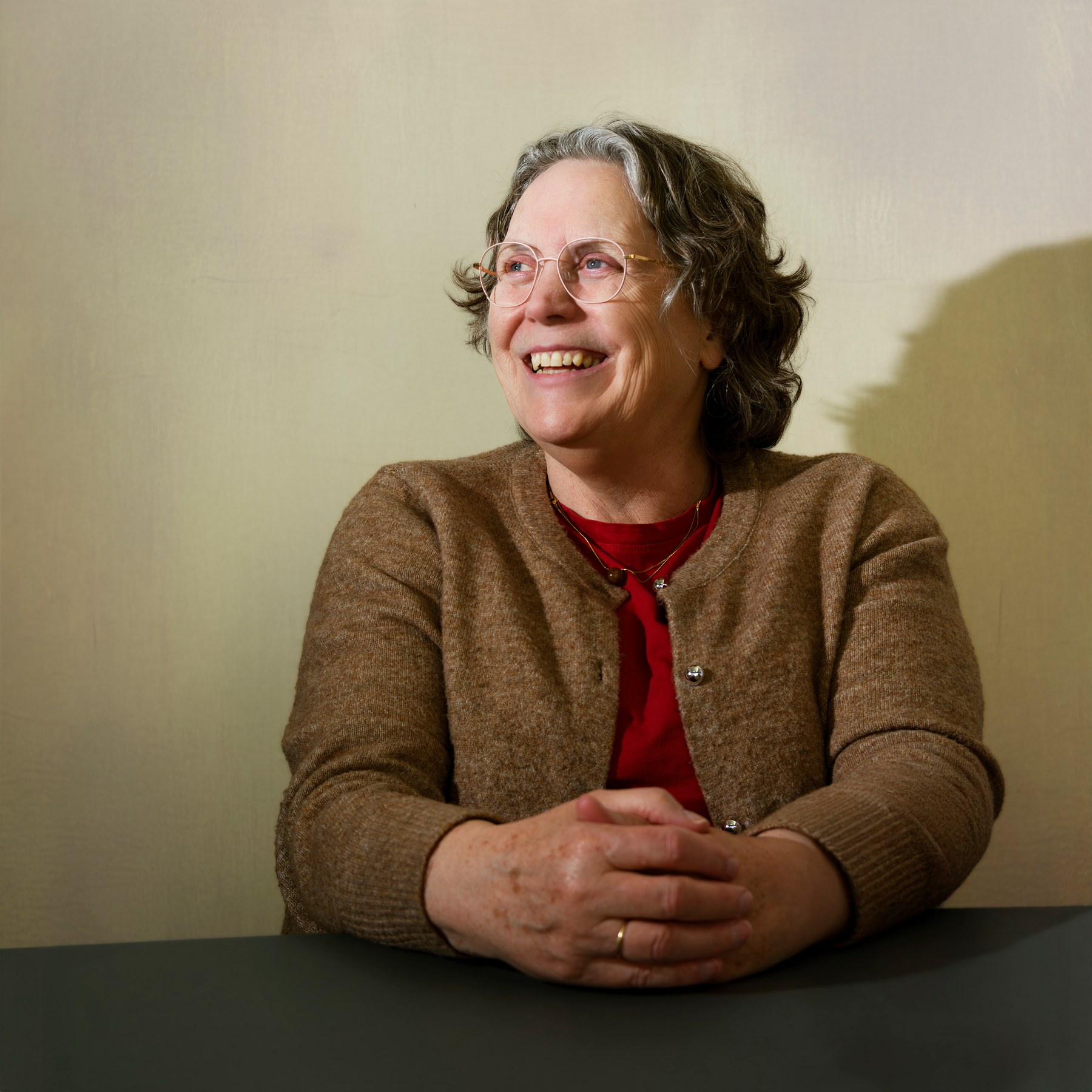 A woman smiling at a table with her hands together.
