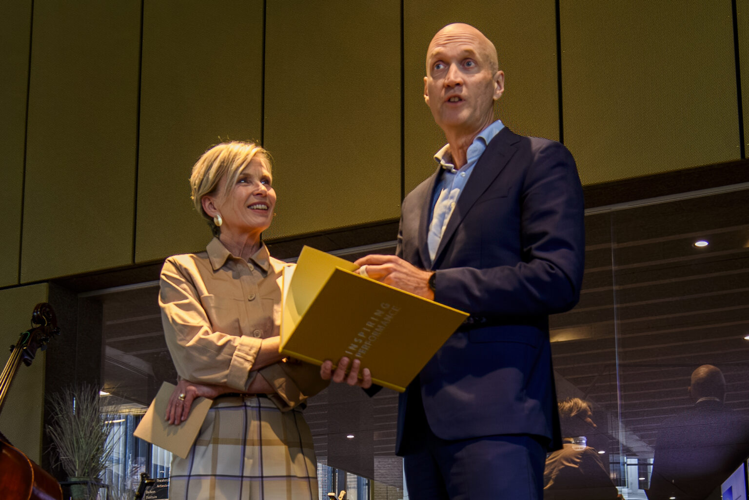 A close view of two presenters holding the yellow Inspiring Performance book on stage.